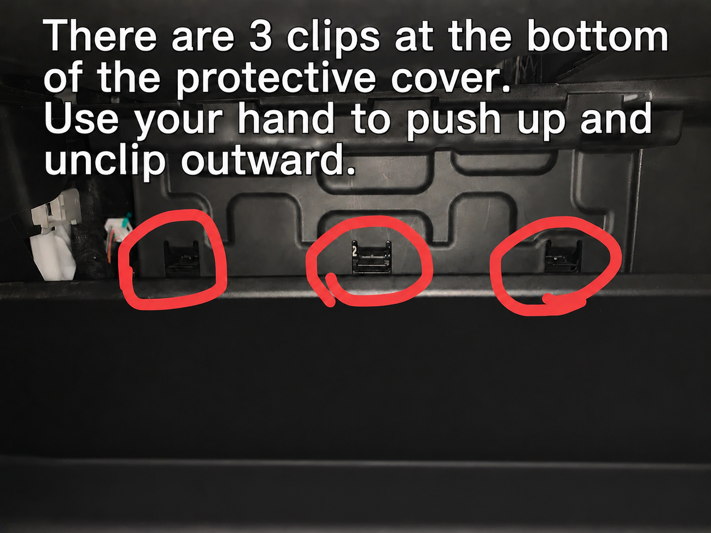 Three plastic retention clips at the bottom edge of the glove box protective cover panel circled in red, demonstrating how to unclip them by pushing up and pulling outward.