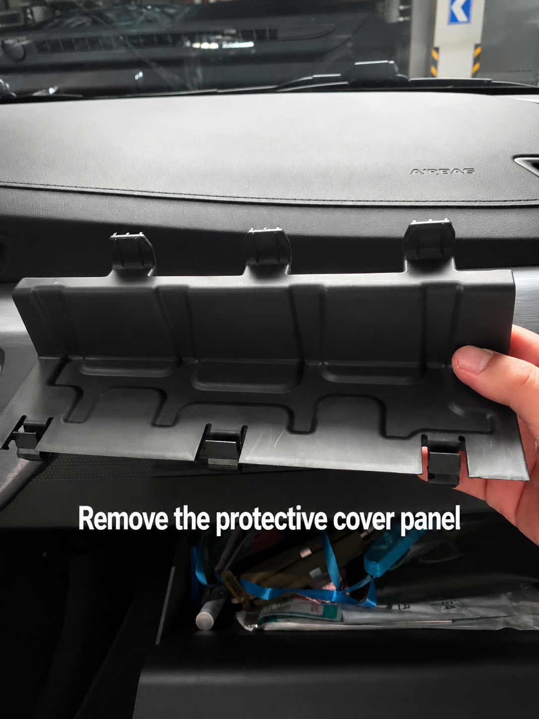 Removing the plastic protective cover panel from behind the passenger glove box to access the cabin air filter housing during a DIY car filter replacement.